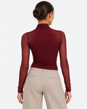 Back view of the Aurore wine red draped mesh long sleeve top styled with beige trousers