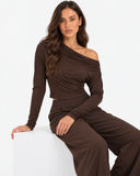 Woman wearing the Eliane brown off-shoulder pleated long-sleeve top, seated front view