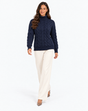 Harriet Dark Blue cable-knit roll-neck jumper, front view with cream trousers and hands beside the hem