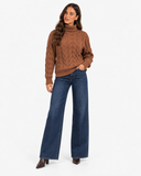 Harriet Light Brown cable-knit roll-neck jumper, three-quarter front styling with one hand in a jeans pocket