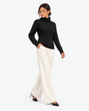 Harriet Black cable-knit roll-neck jumper, full-length styling with one hand in a trouser pocket