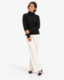 Harriet Black cable-knit roll-neck jumper, three-quarter front view with cream trousers