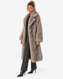 Full-length three-quarter view of the Claudine taupe faux-fur coat, worn open with black trousers.