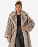 Closer front view of the Claudine taupe faux-fur coat, with one hand on the hip.