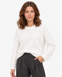 White round-neck knit sweater shown in a close front view with charcoal trousers.