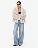 Solenne ivory faux-fur jacket worn with arms crossed and blue jeans