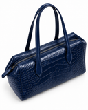 Rear three-quarter view of a dark blue crocodile-pattern tote bag showing the top zip and handle attachments.