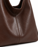 Close-up of the brown faux leather shoulder bag showing the central stitched seam and textured finish.