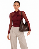 Model in a burgundy long-sleeve top and beige trousers carrying the brown faux leather shoulder bag.